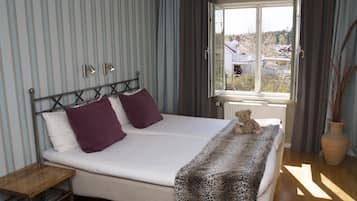 Un dormitorio con cama, mesita de noche, ventana con cortinas y vistas al exterior.