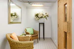 Una habitación con una silla de mimbre, una mesita, un espejo y un jarrón con flores.
