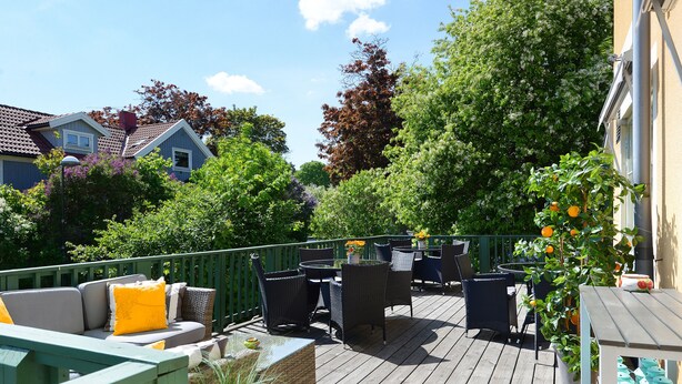 Una terraza de madera con mobiliario exterior, rodeada de abundante vegetación y árboles.