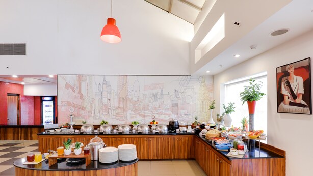 A modern hotel lobby with a breakfast bar, wooden cabinets, and a cityscape mural.