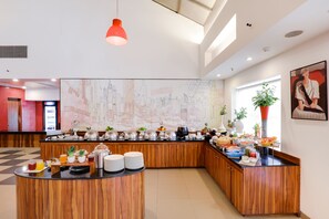 Un hall d’hôtel moderne avec un buffet pour le petit-déjeuner, des meubles en bois et une fresque représentant un paysage urbain.