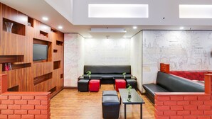 A modern lounge area with wooden paneling, a black sofa, red and black ottomans, and a flat-screen TV mounted on the wall.