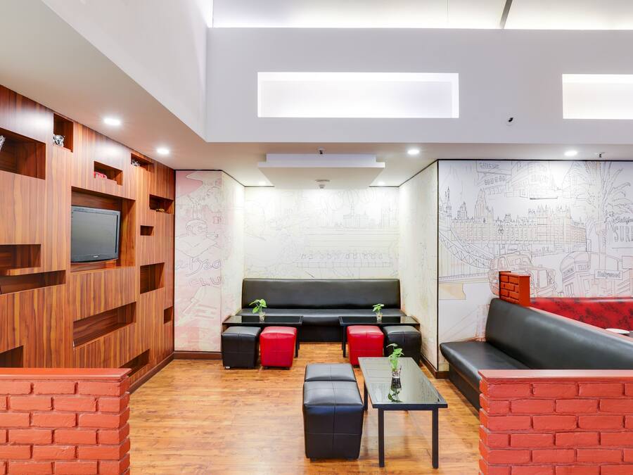 A modern lounge area with wooden paneling, a black sofa, red and black ottomans, and a flat-screen TV mounted on the wall.