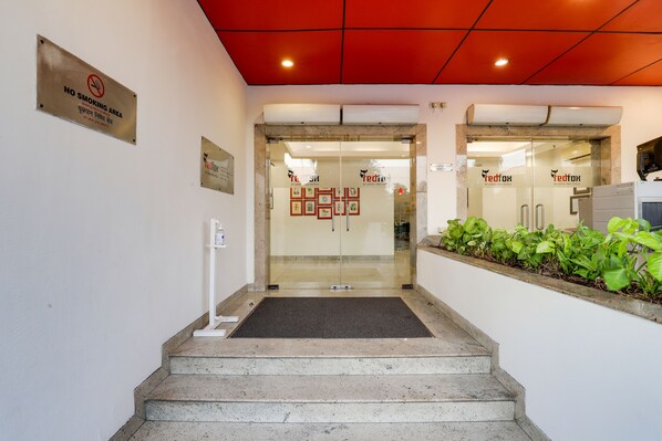 L’entrée d’un hôtel, avec un panneau « interdiction de fumer », une porte en verre et une petite marche menant à l’entrée.