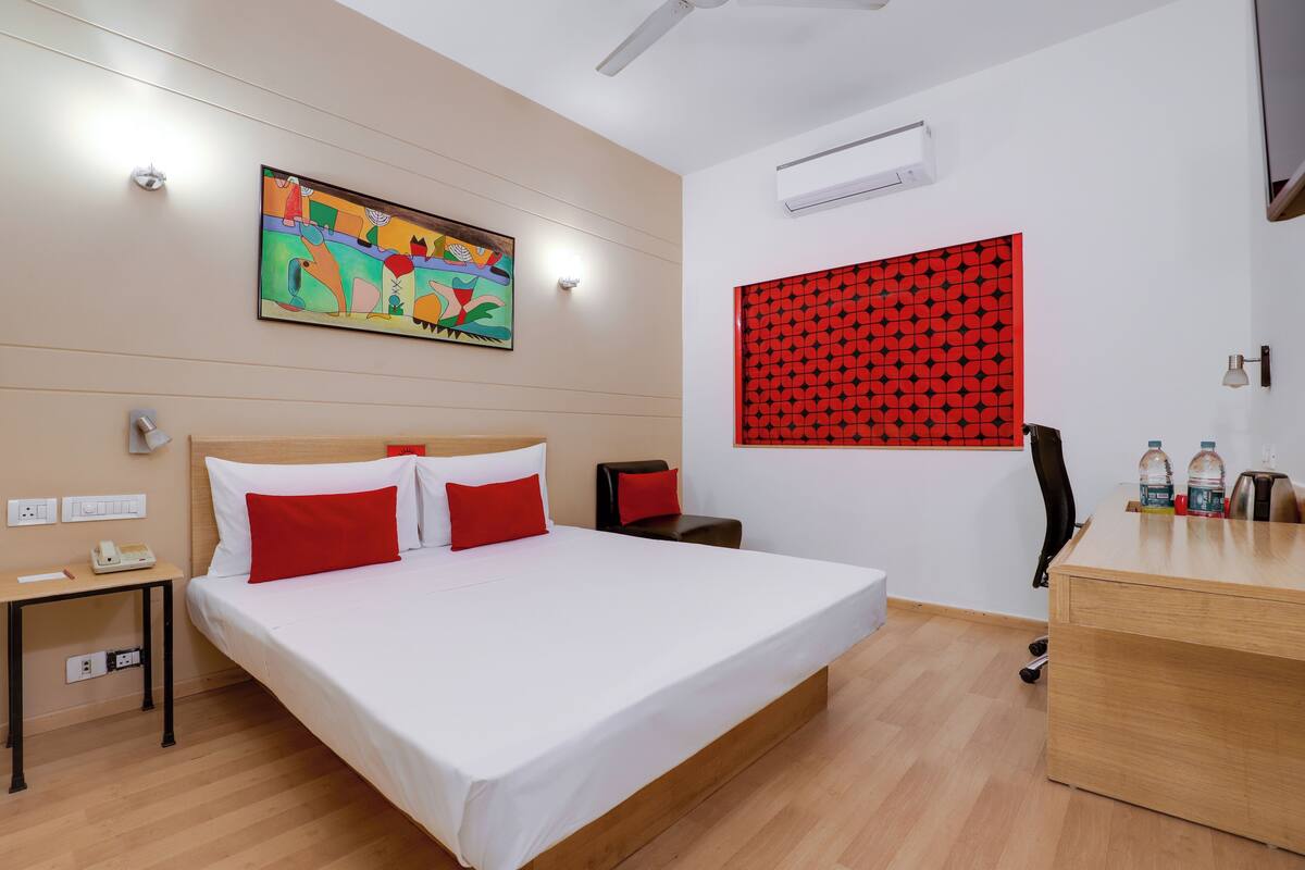 A hotel room with a bed, a desk, a chair, a painting, and a patterned wall.