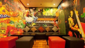A vibrant room with a sofa and ottomans, a piano, and colorful murals on the walls.