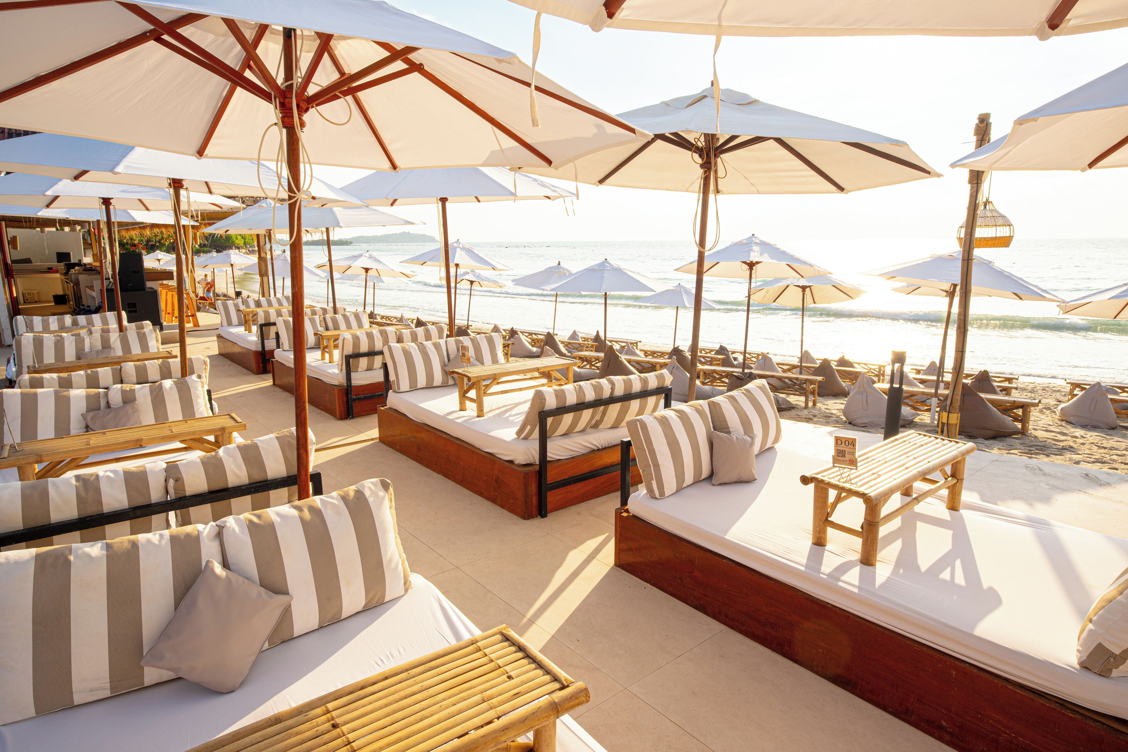 A beachside lounge with multiple seating areas, including sofas and chairs, under large umbrellas.