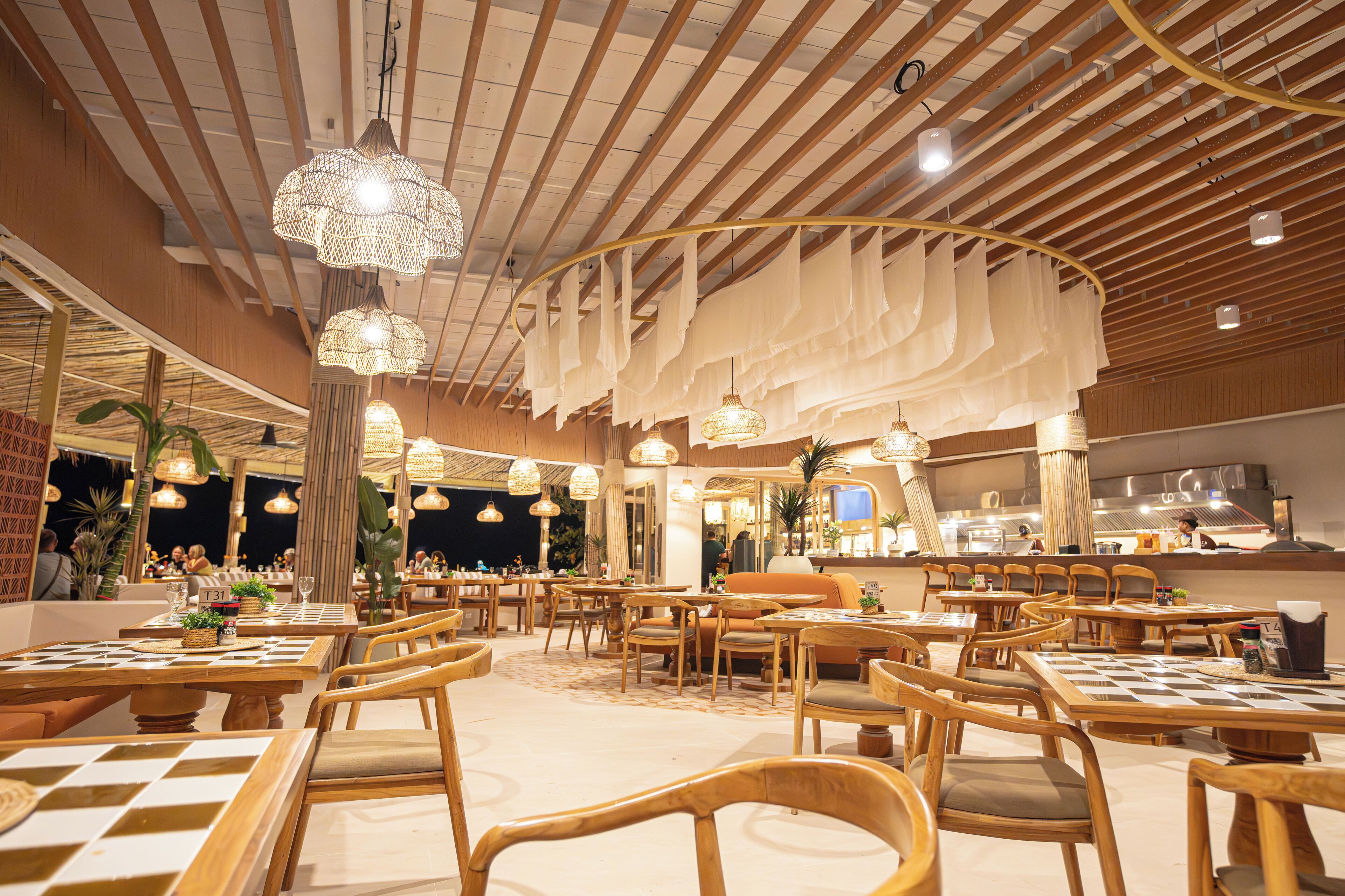 A spacious restaurant with wooden furniture, hanging lights, and a high ceiling.