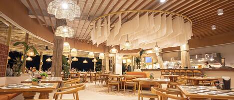 A spacious restaurant with wooden furniture, hanging lights, and a high ceiling.