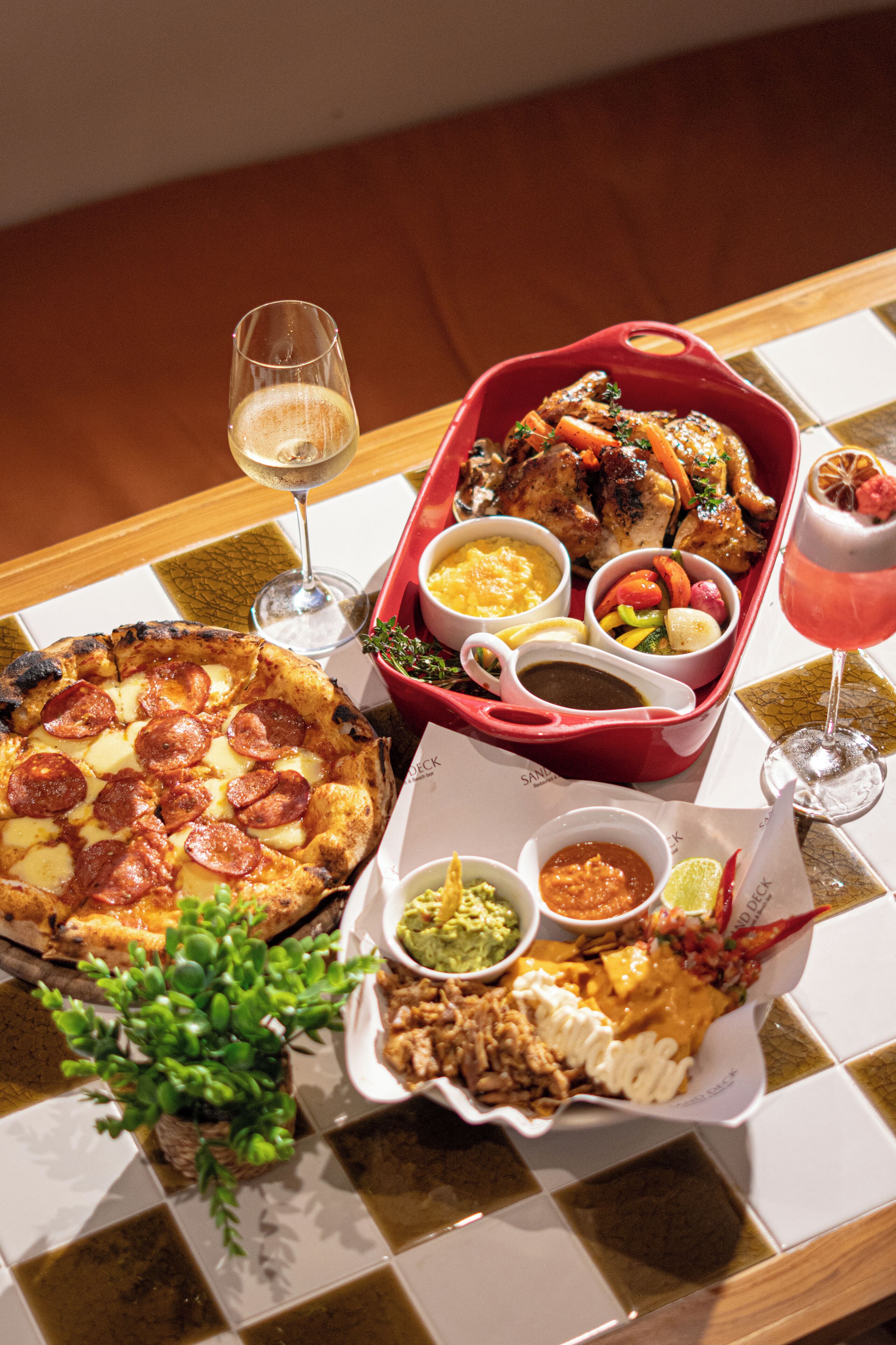 A table with a variety of dishes including pizza, a red baking dish with meat, and several small bowls of sauces and dips.