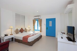 Quarto de hotel com cama, luminárias de cabeceira, escrivaninha com telefone, televisão e porta azul.