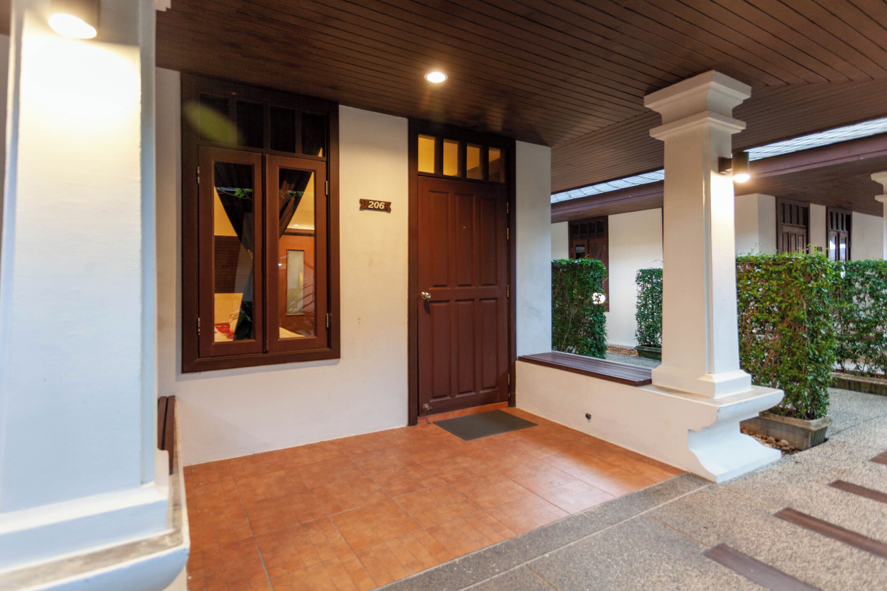 A hotel entrance with a wooden door, a number plaque, and a tiled floor.