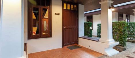 A hotel entrance with a wooden door, a number plaque, and a tiled floor.