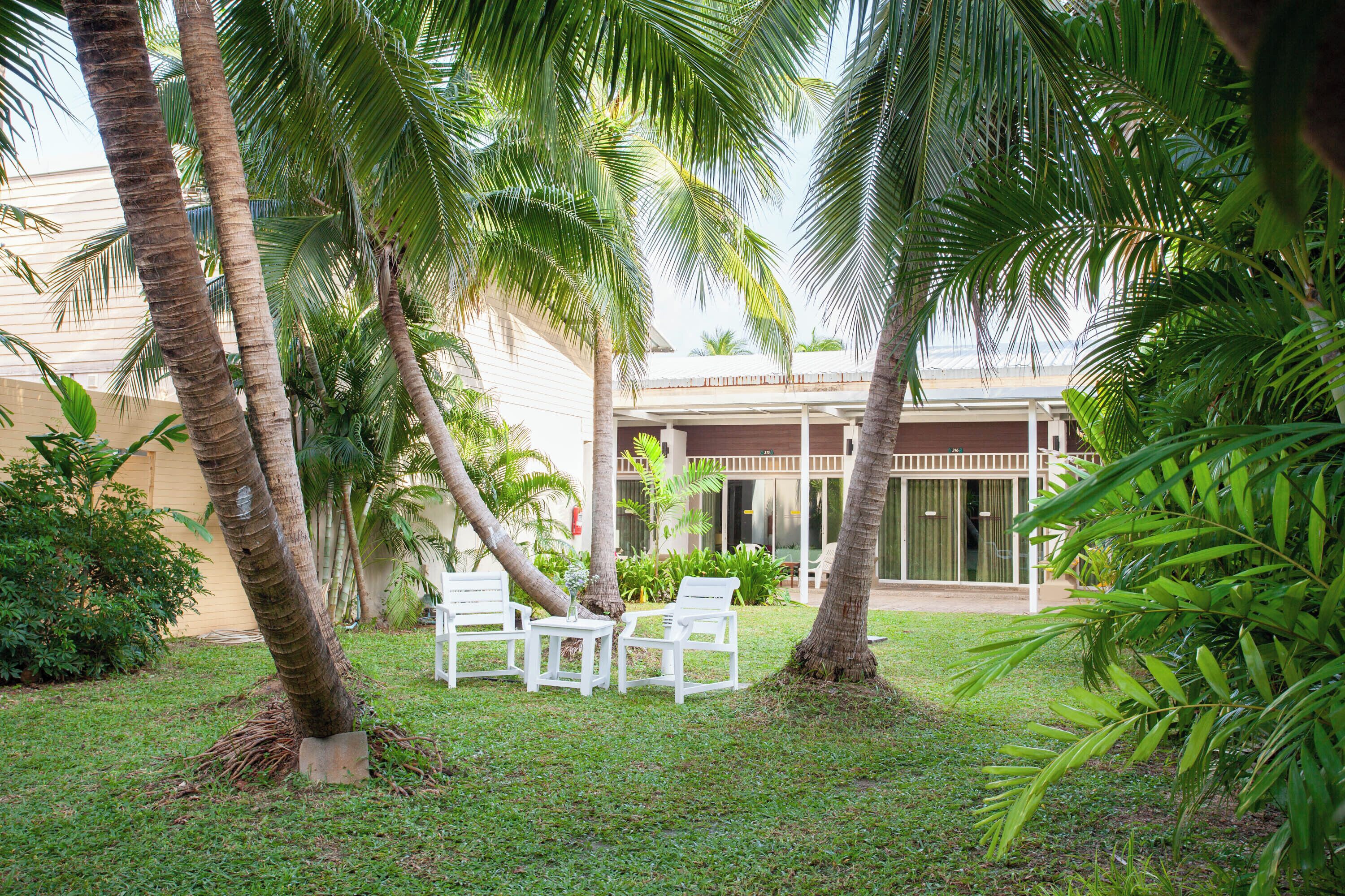 Un patio con palmeras, una zona de estar cubierta y un edificio con grandes ventanales.