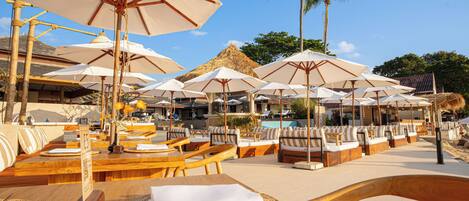 Ein Restaurant direkt am Strand mit Terrassenplätzen, Sonnenschirmen und einem Pool.