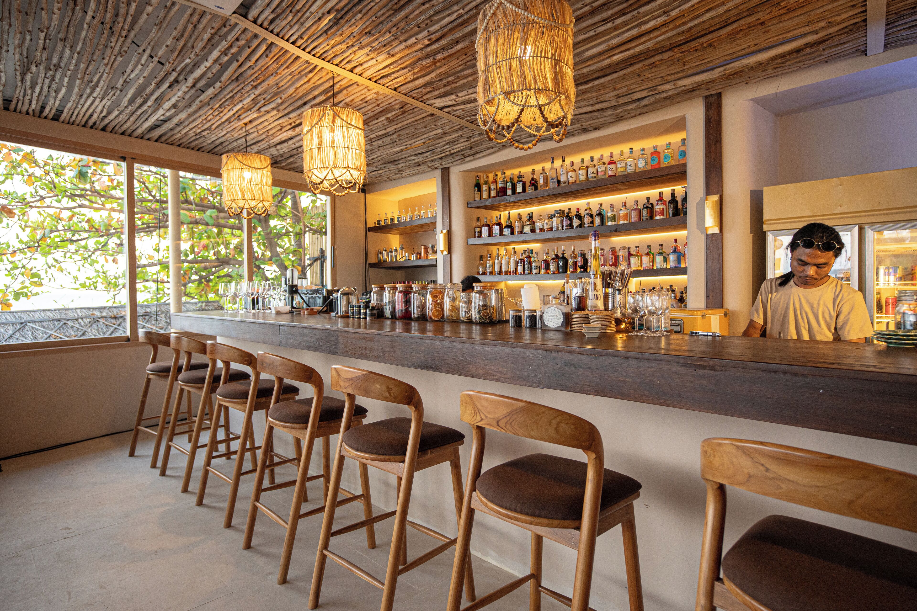 A bar area with wooden chairs, a bar counter, and shelves of liquor bottles.