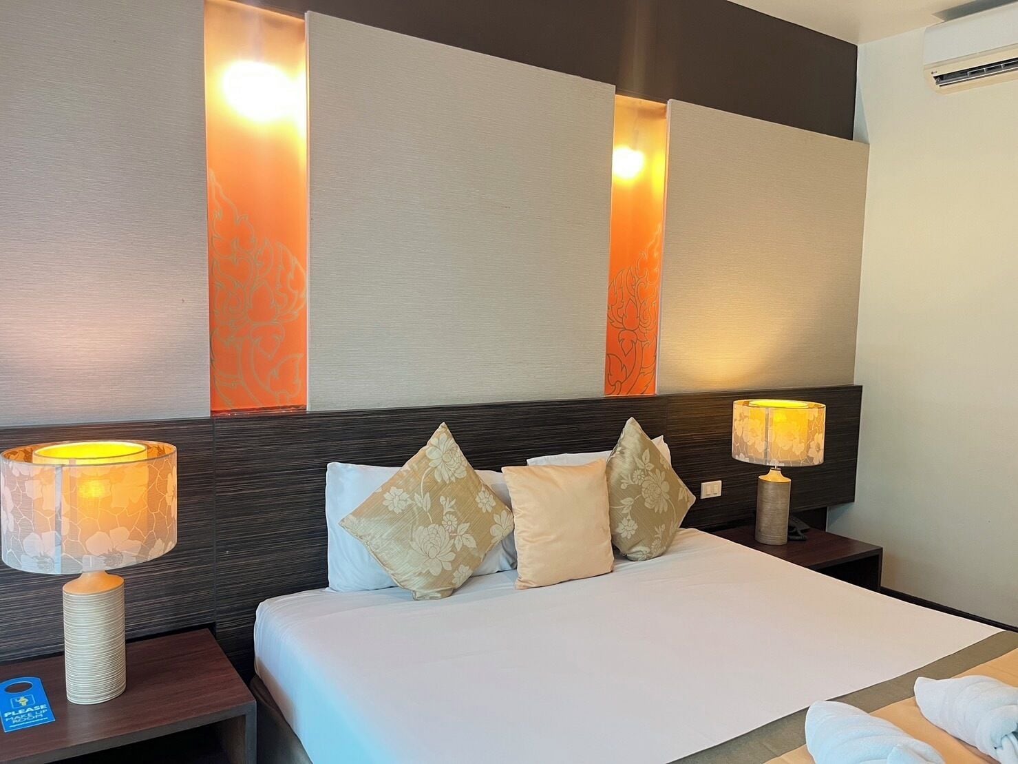 A hotel room with a neatly made bed, two bedside lamps, and a wall with vertical light panels.