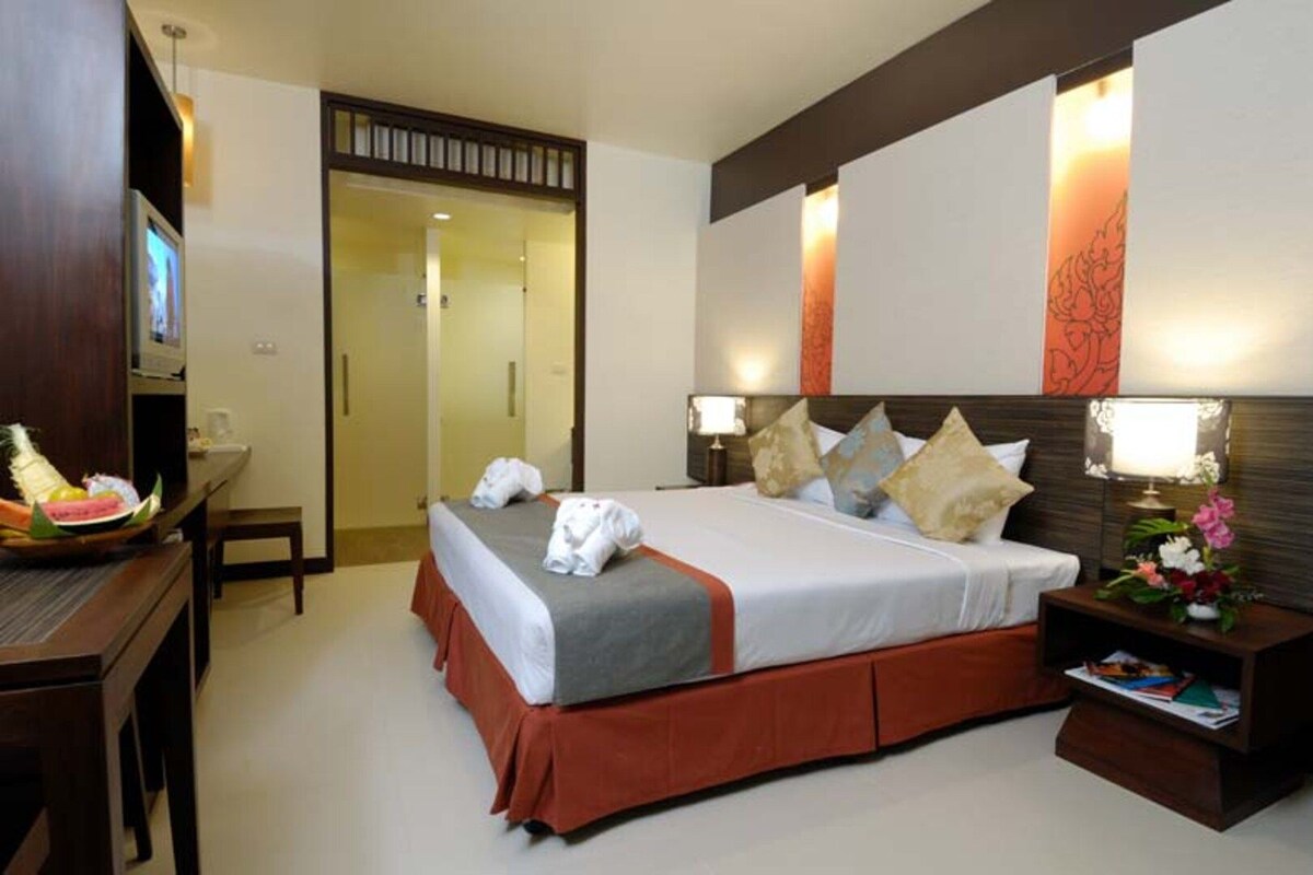 A hotel room with a bed, bedside tables, a desk with a chair, and a television.