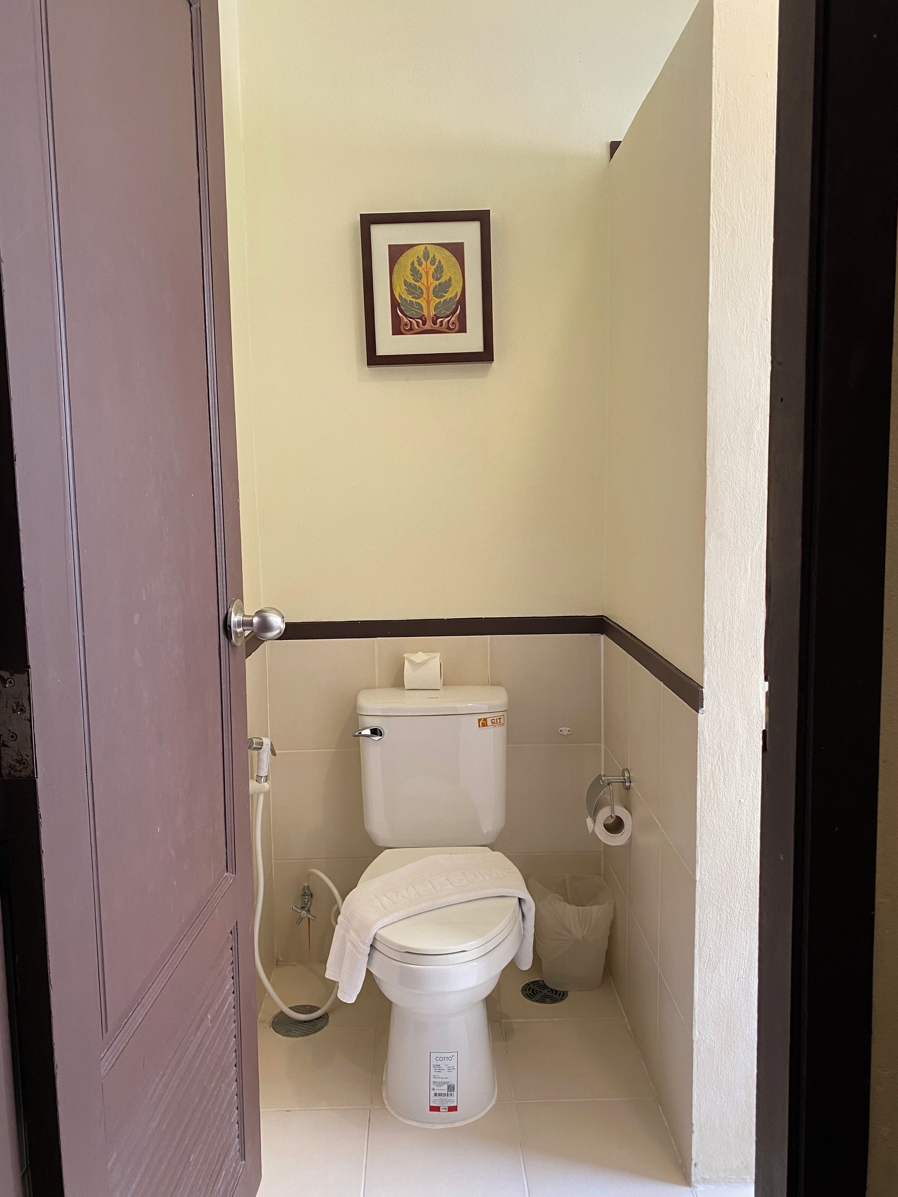 A small, compact bathroom with a toilet, a towel on the seat, and a framed picture on the wall.