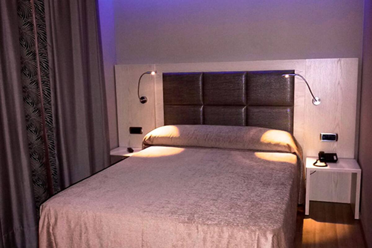 A modern hotel room with a large bed, wooden flooring, and a headboard with built-in lighting.