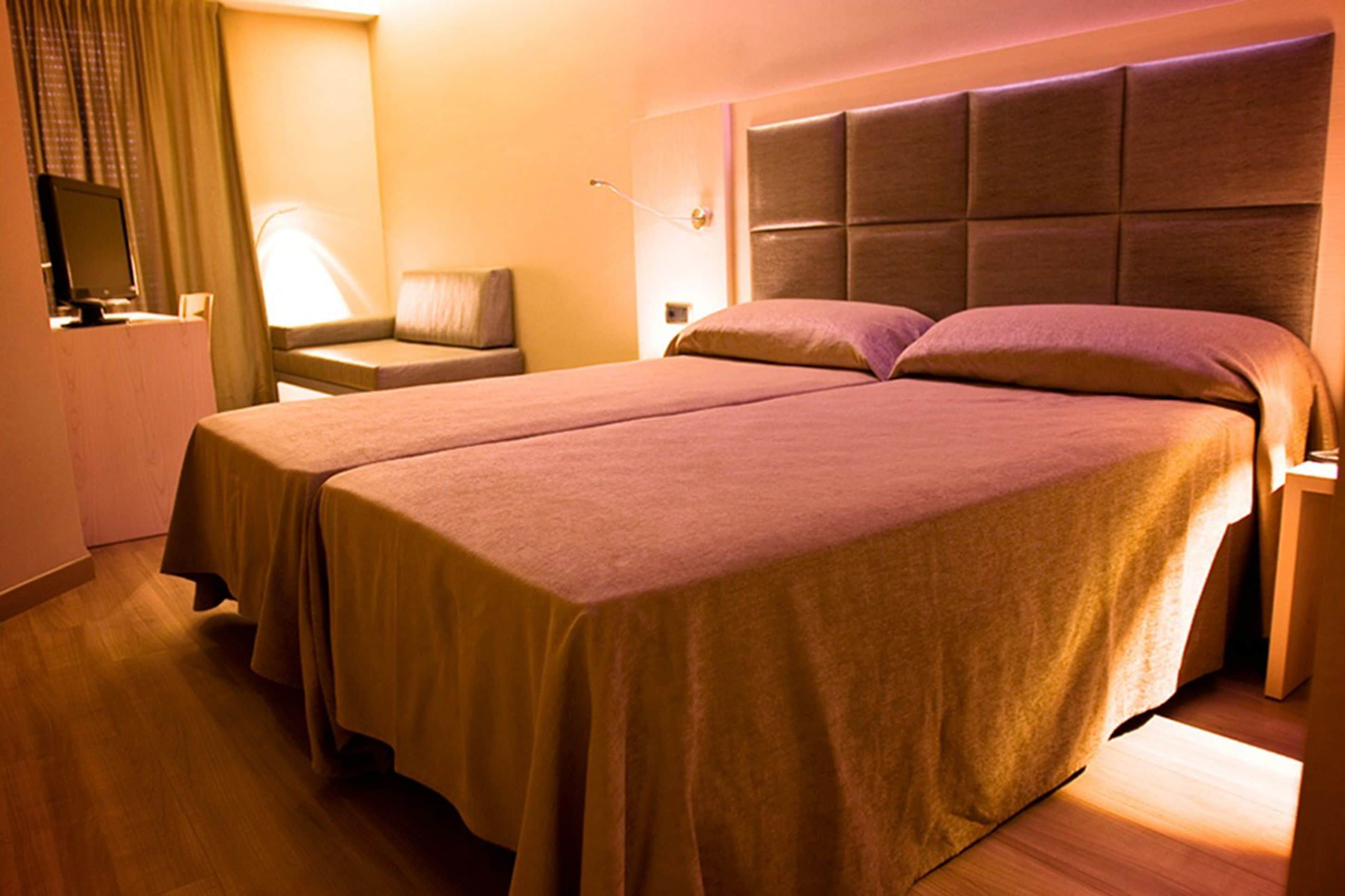 A hotel room with a large bed, a bedside table, a lamp, and a television on a stand.