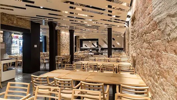A modern restaurant with wooden tables and chairs, a stone wall, and a contemporary ceiling design. - Hotel Barcelona House (Barcelona)