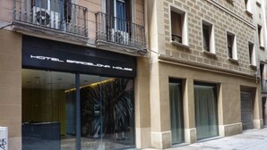 A hotel facade with a modern glass entrance, a large window with a decorative pattern, and a balcony with metal railings. - Hotel Barcelona House (Barcelona)