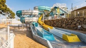 A water park with multiple water slides and a stone wall. - Guitart Central Park Aqua Resort (Lloret de Mar)
