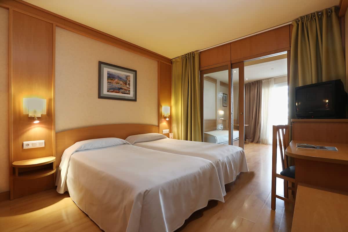 Ein Hotelzimmer mit zwei Betten, einem Schreibtisch, einem Fernseher und einem Fenster mit Vorhängen.