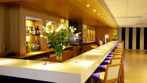 A bar area with a long counter, multiple liquor bottles, and a vase with flowers. - Guitart Central Park Aqua Resort (Lloret de Mar)