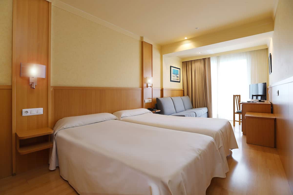 Ein Hotelzimmer mit zwei Betten, einem Schreibtisch, einem Stuhl und einem Fernseher.