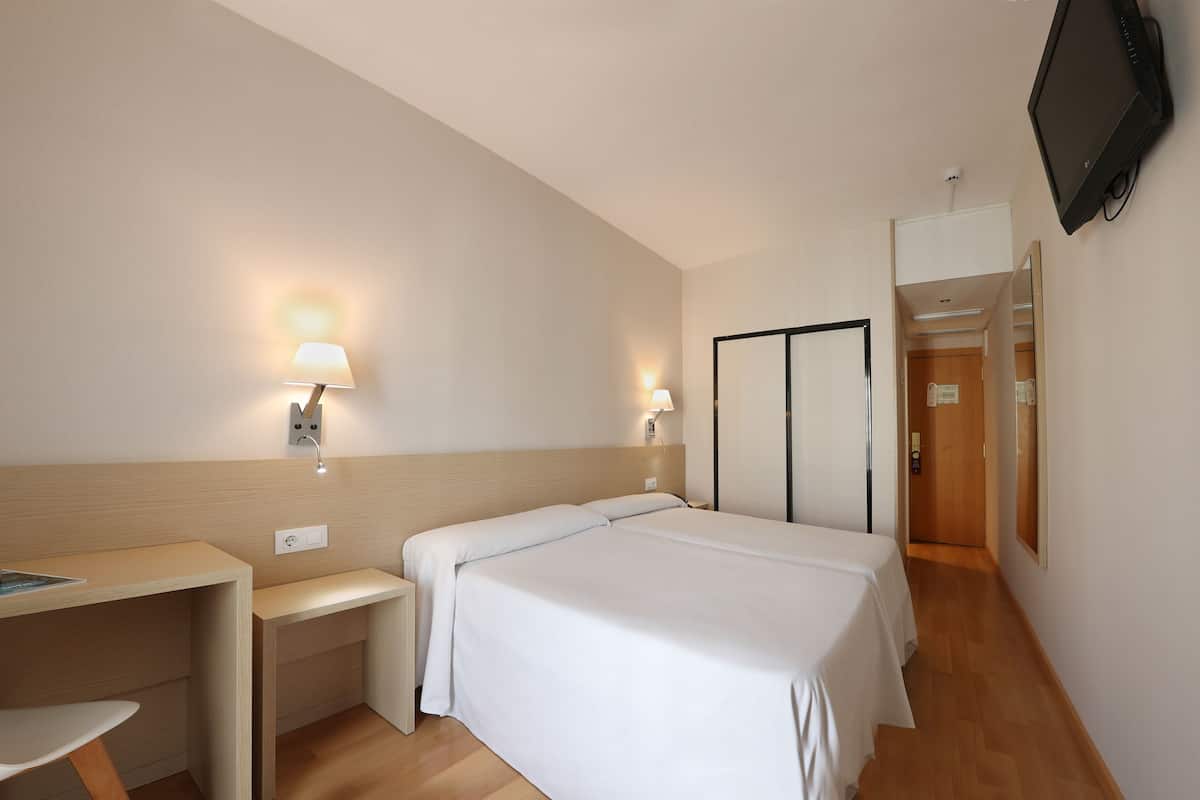Ein Hotelzimmer mit Bett, Schreibtisch, Stuhl, Fernseher und einer Tür.