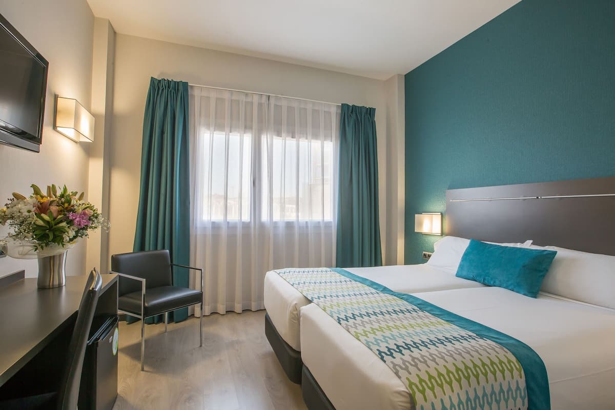 Een hotelkamer met een bed, een bureau, een stoel en een raam met gordijnen.
