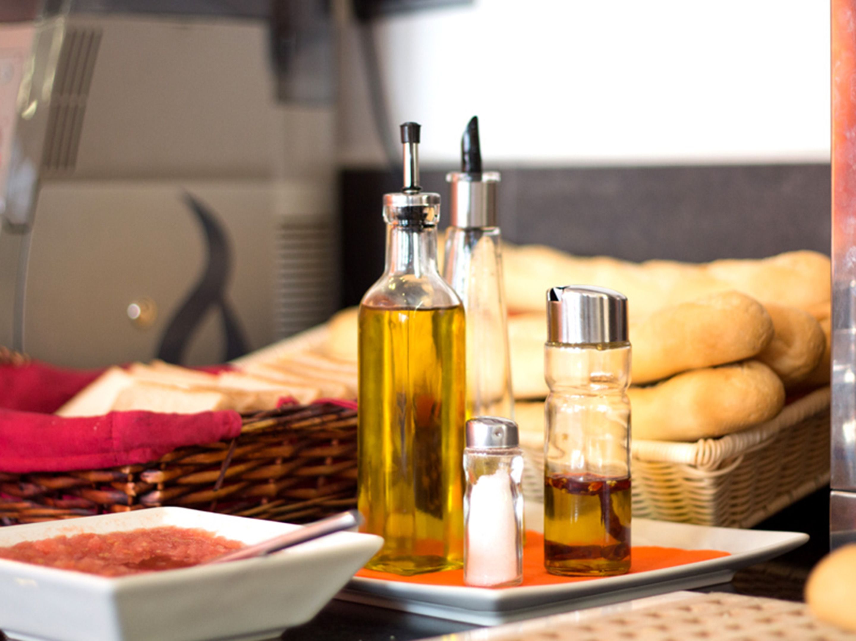 Una mesa con diferentes condimentos, incluyendo una botella de aceite, un salero y un pimentero, junto con un cesto de pan.