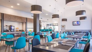 A modern dining area with blue chairs and tables, a coffee machine, and a TV on the wall. - Hotel Venture Sant Cugat (Sant Cugat del Valles)