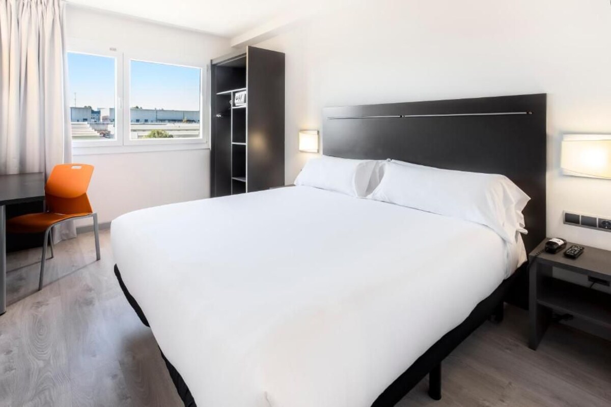 Habitación de hotel con una cama grande, un escritorio, una silla, un armario y una ventana con vistas.