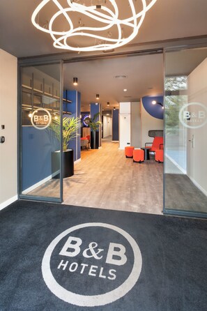 A modern hotel lobby with a B&B logo on the carpet, a reception desk, and seating areas. - B&B Hotel Barcelona Rubí (Rubi)