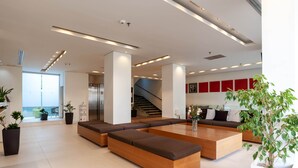 Un vestíbulo moderno con una zona de estar central, una escalera y un mostrador de recepción.