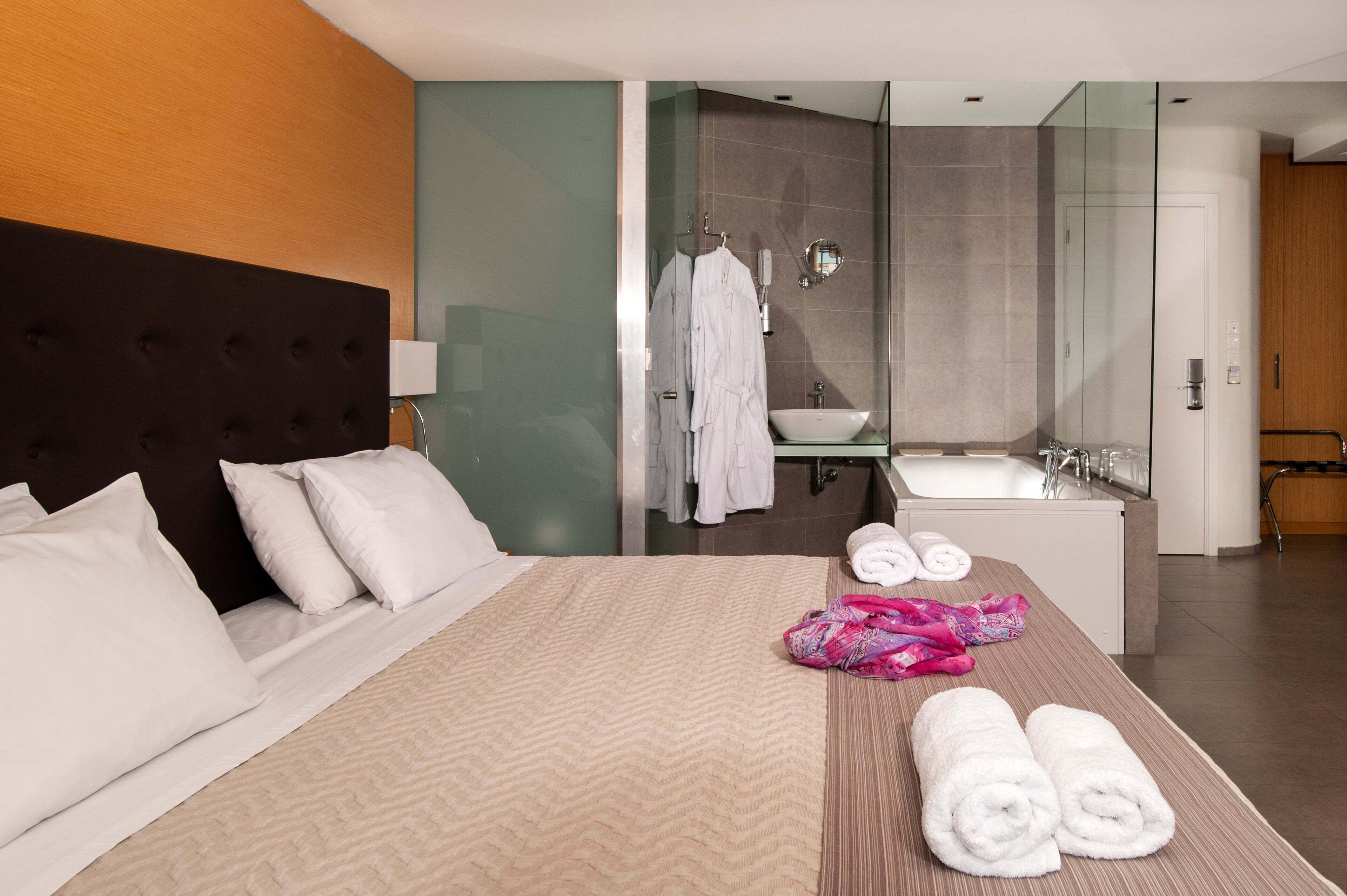 A hotel room with a bed, a bathroom with a sink and mirror, and towels on the bed.