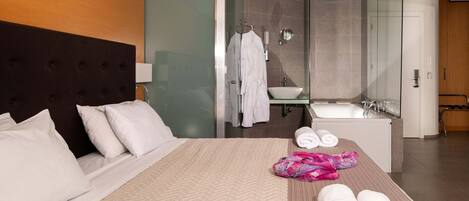 A hotel room with a bed, a bathroom with a sink and mirror, and towels on the bed.