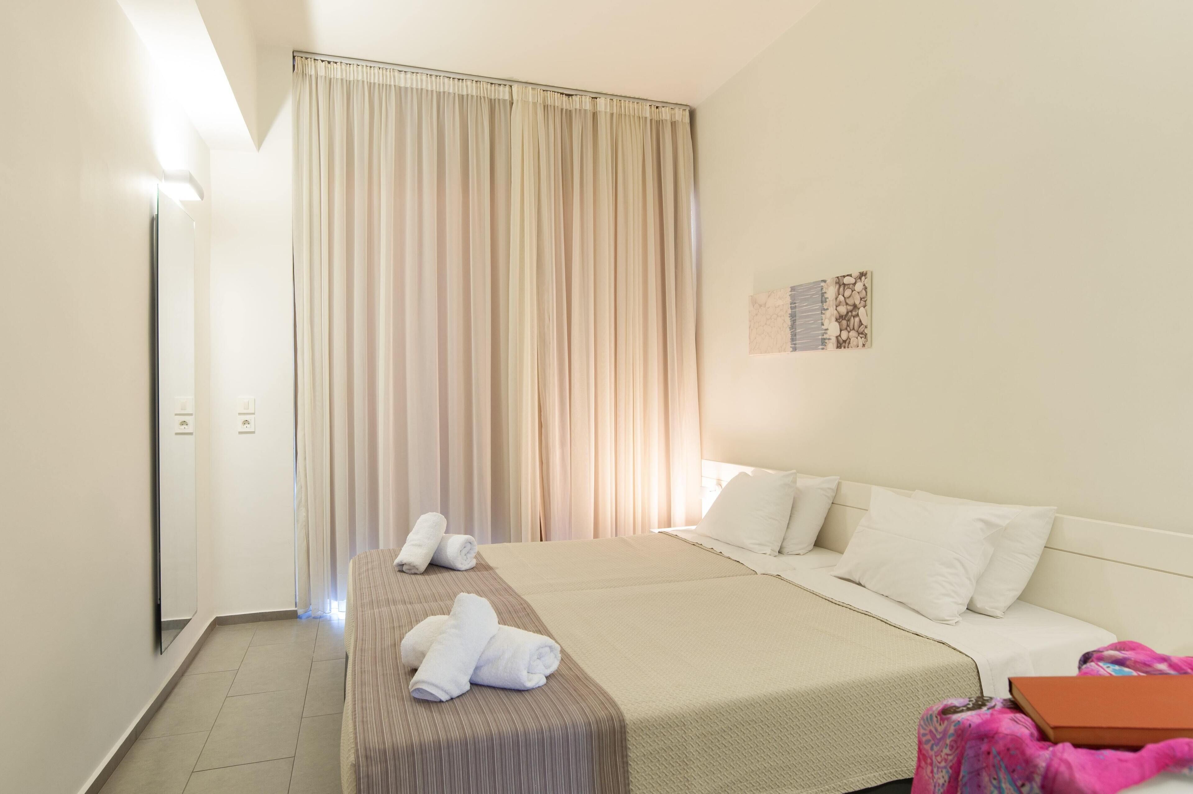 A hotel room with a bed, a bedside table, a mirror, a window with curtains, and a wall art piece.