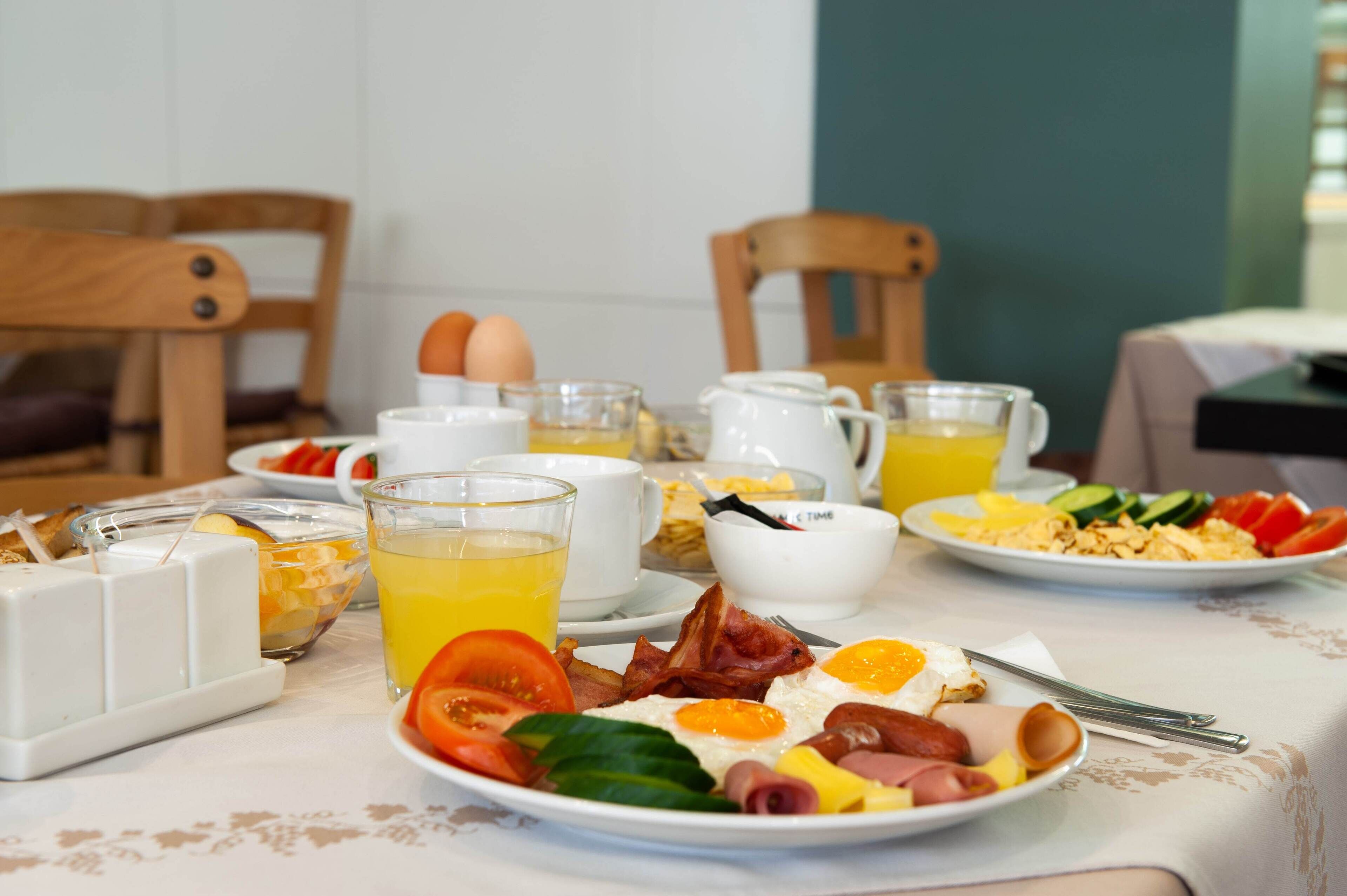 A breakfast setting with plates of eggs, bacon, tomatoes, and other breakfast items, along with glasses of orange juice and a pitcher.