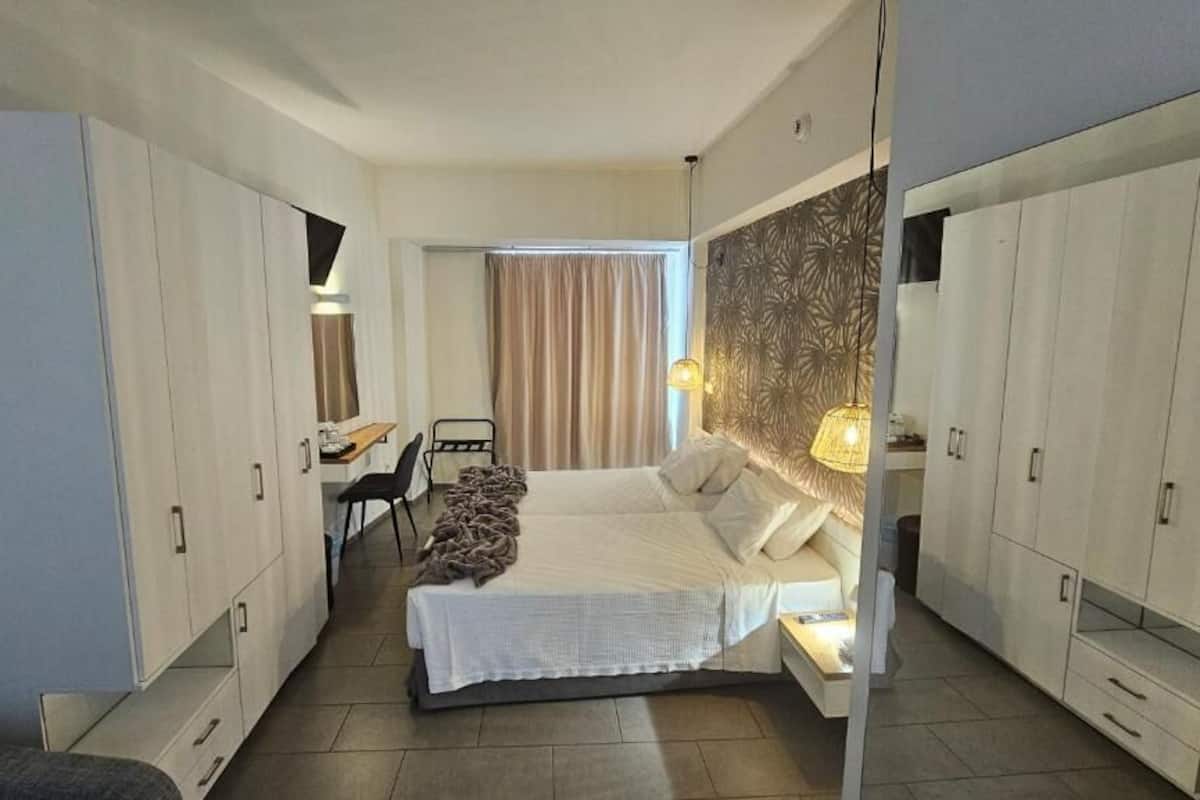 Ein Hotelzimmer mit Bett, Schreibtisch, Stuhl, Kleiderschrank und einem großen Fenster mit Vorhängen.
