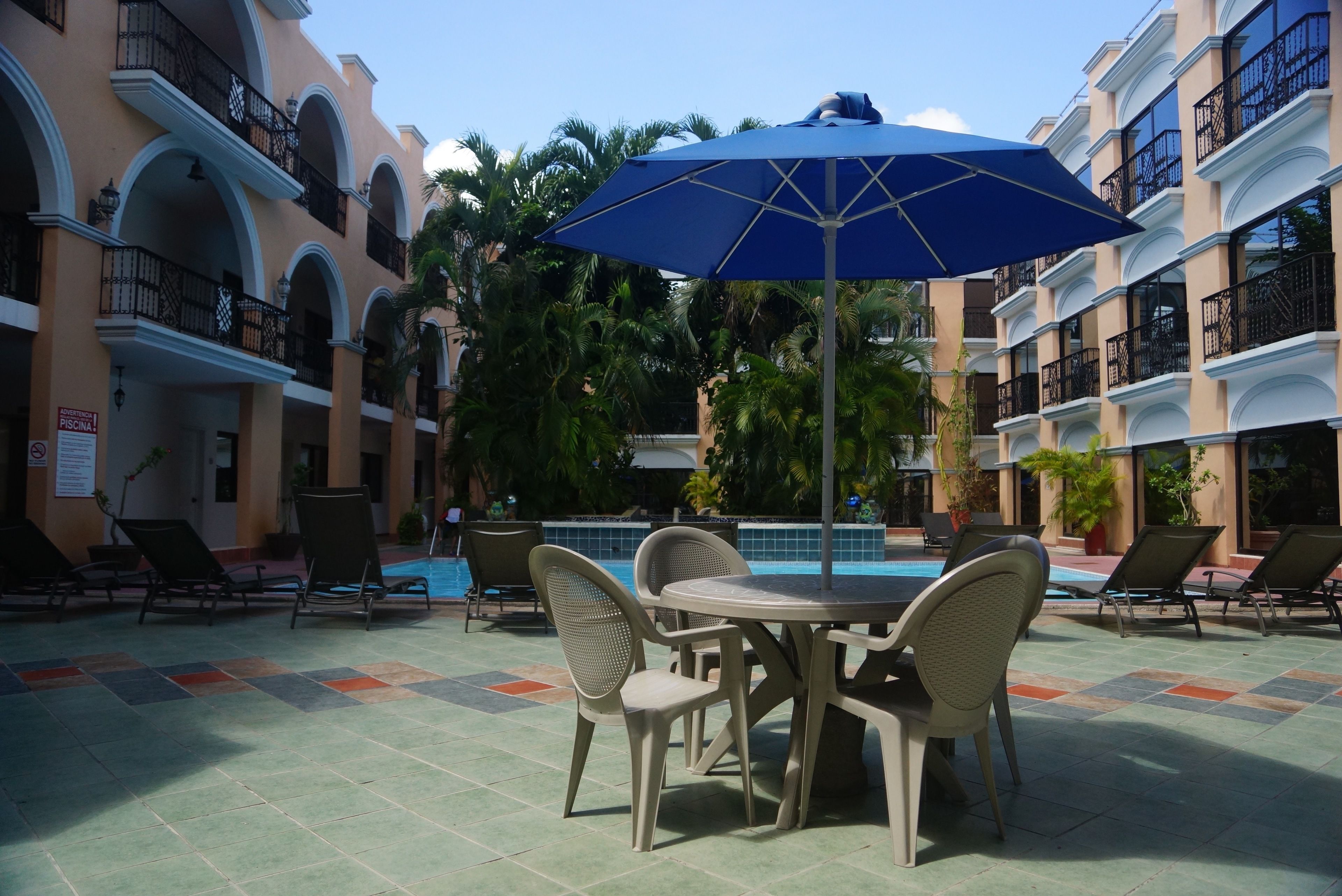 Un área junto a la piscina con sillas de descanso, una mesa y una sombrilla azul.