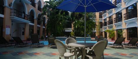Un área junto a la piscina con sillas de descanso, una mesa y una sombrilla azul.