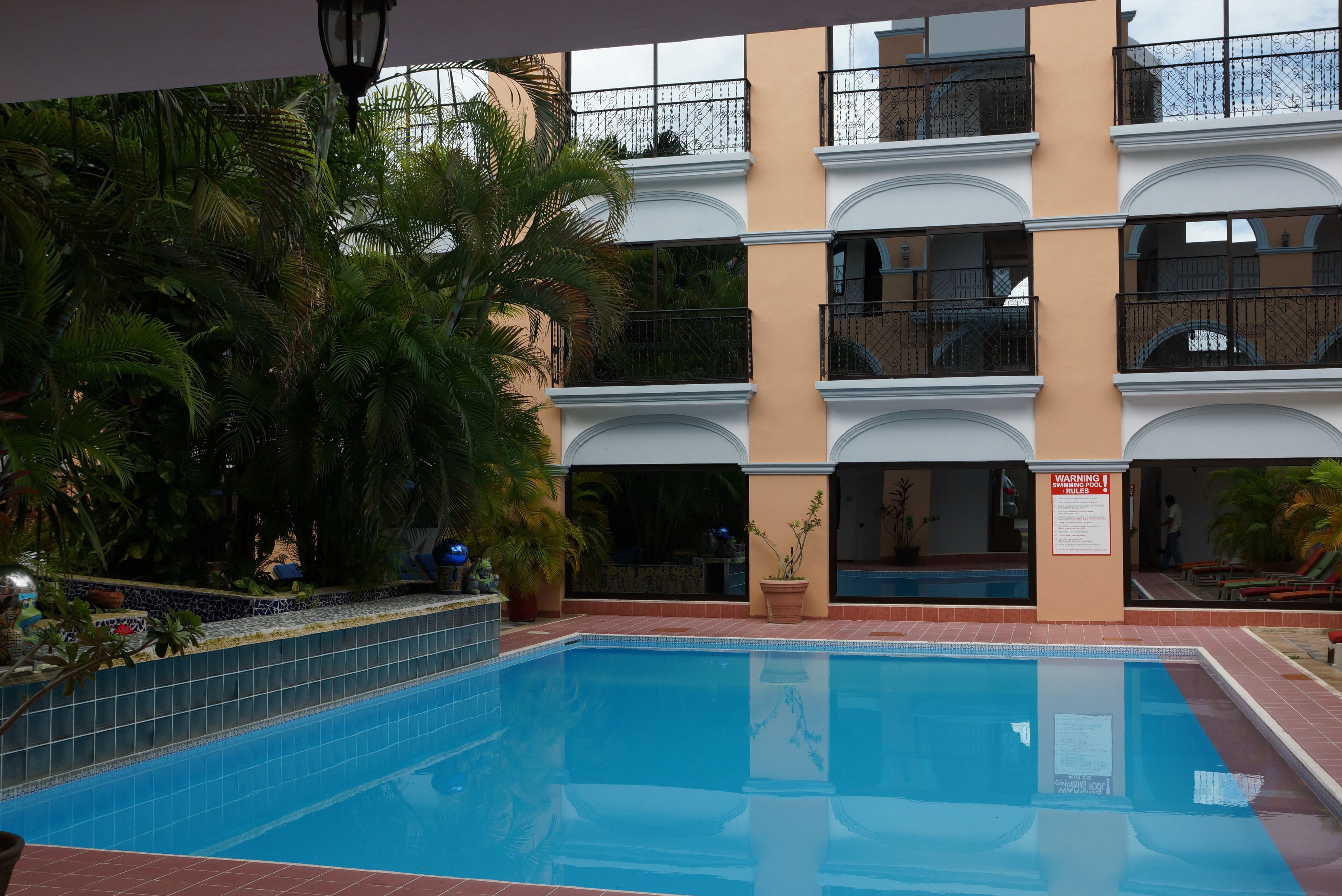 A swimming pool with a tiled edge, surrounded by a building with multiple balconies and a tiled roof.