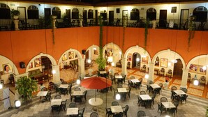 A courtyard with multiple dining tables and chairs, surrounded by arches and potted plants. - Hotel Doralba Inn (Mérida)