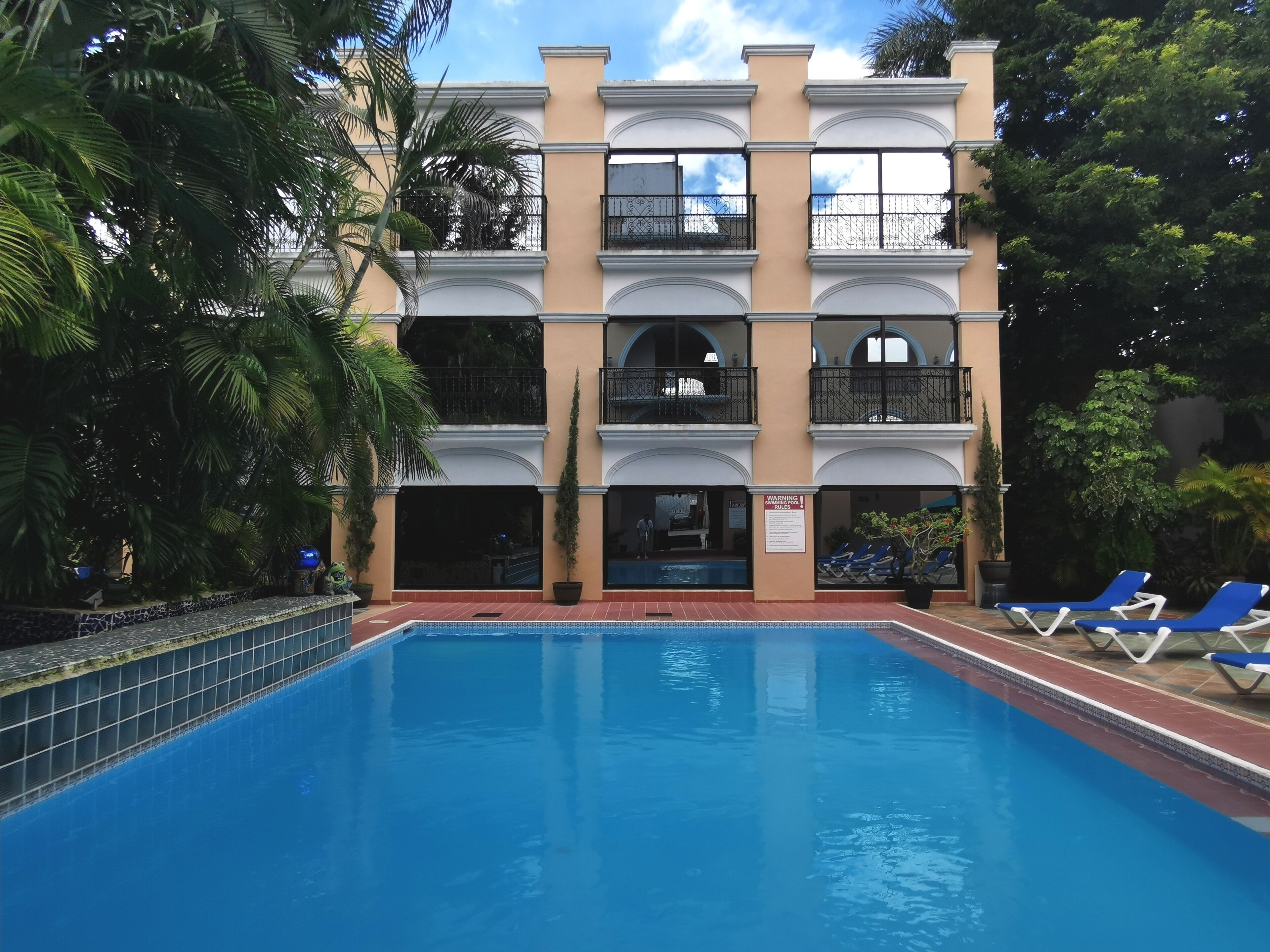 Un hotel de varios pisos con piscina, balcones y abundante vegetación.