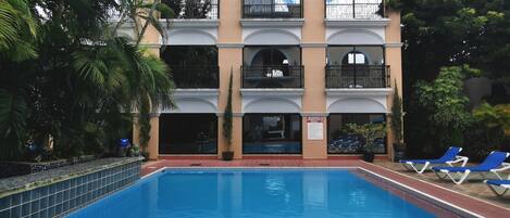Un hotel de varios pisos con piscina, balcones y abundante vegetación.