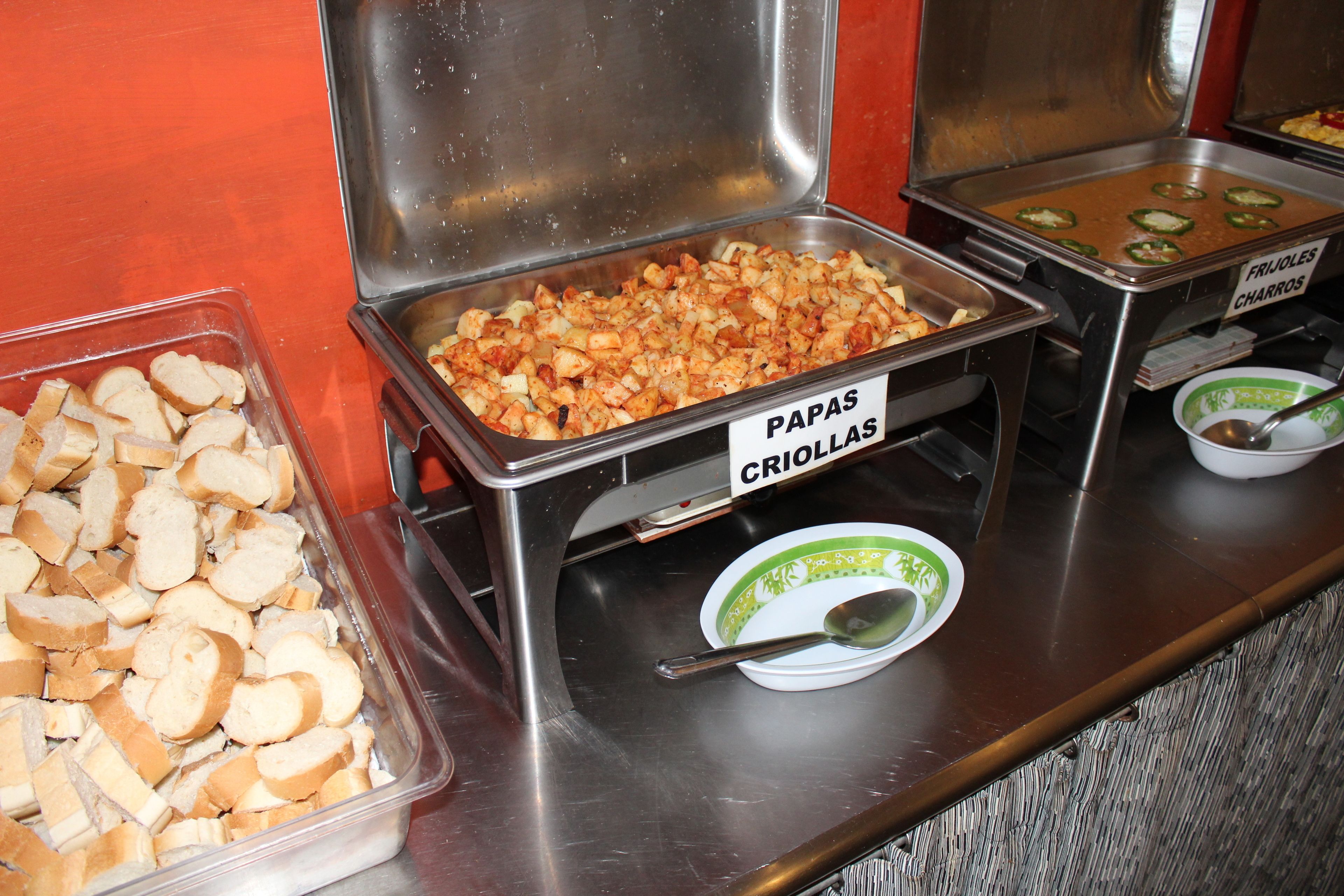 A buffet with labeled food items including papas criollas, charros, and bread.